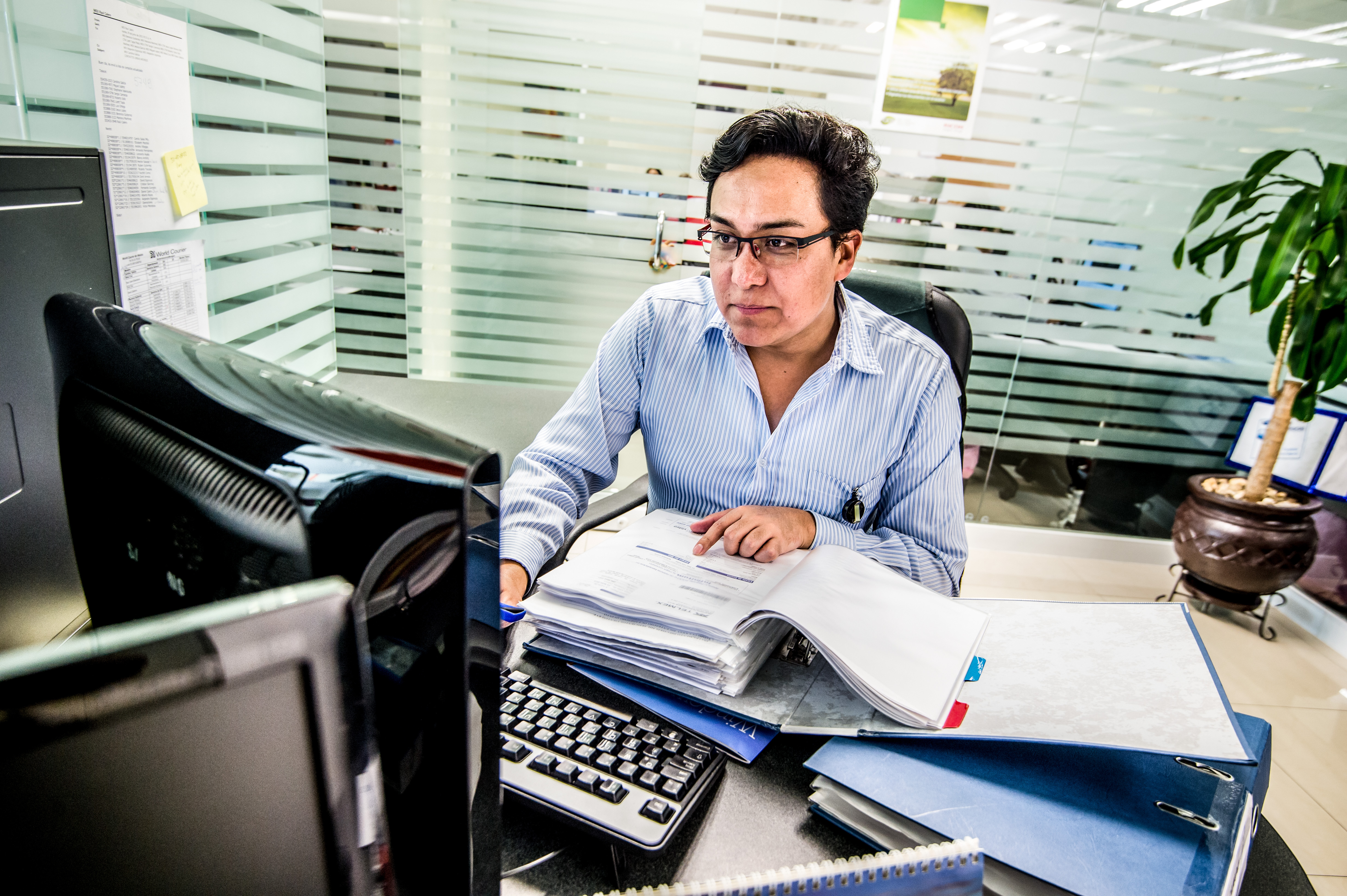 An associate works at a computer with a large binder open on the desk.