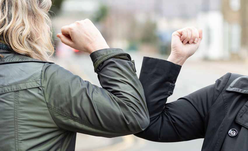 two women bumping elbows to greet each other